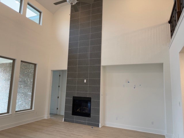 unfurnished living room with a tiled fireplace, high vaulted ceiling, light hardwood / wood-style floors, and ceiling fan