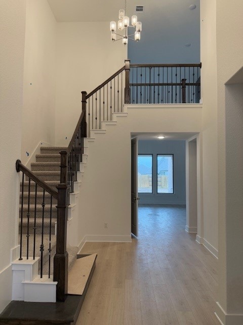 stairway with an inviting chandelier, wood-type flooring, and a high ceiling