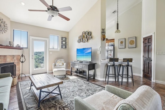 living room with a tiled fireplace, ceiling fan, and high vaulted ceiling