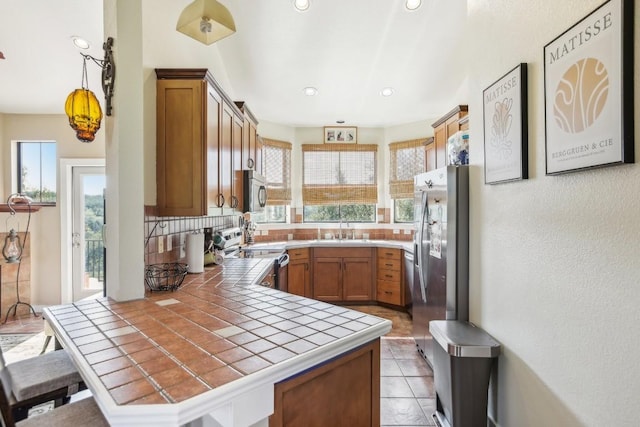 kitchen featuring kitchen peninsula, backsplash, stainless steel appliances, pendant lighting, and tile counters