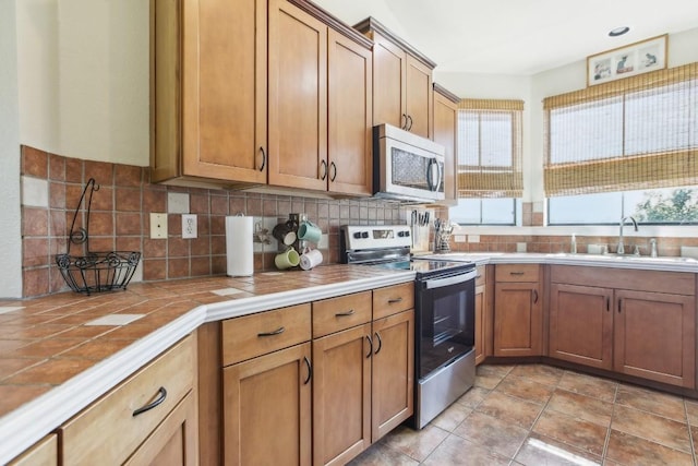 kitchen featuring decorative backsplash, appliances with stainless steel finishes, sink, light tile patterned floors, and tile counters