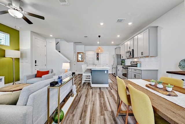 kitchen featuring a kitchen breakfast bar, hanging light fixtures, a kitchen island with sink, gray cabinetry, and appliances with stainless steel finishes