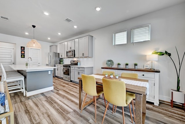 kitchen with gray cabinetry, stainless steel appliances, an island with sink, and decorative light fixtures