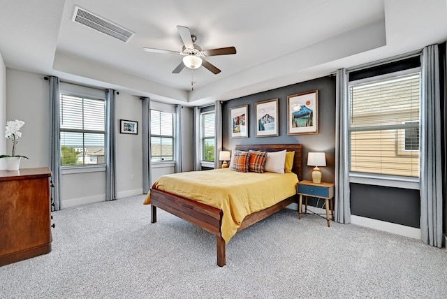 bedroom with ceiling fan, light carpet, and a tray ceiling