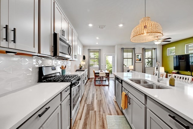 kitchen with stainless steel appliances, sink, ceiling fan, tasteful backsplash, and pendant lighting