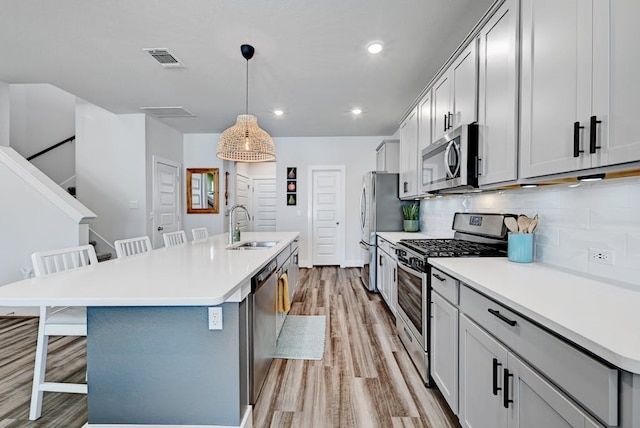 kitchen featuring a breakfast bar area, stainless steel appliances, an island with sink, sink, and decorative light fixtures