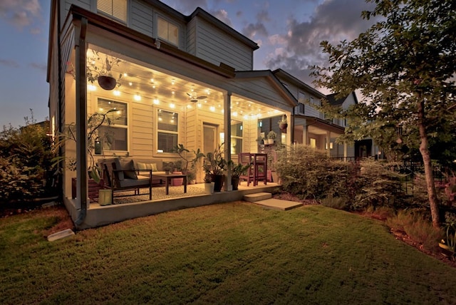 back house at dusk with ceiling fan and a lawn