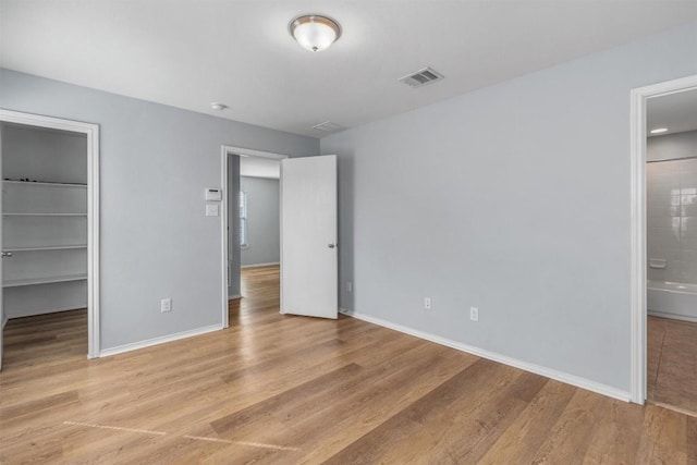 unfurnished bedroom with a closet, a walk in closet, ensuite bathroom, and light wood-type flooring