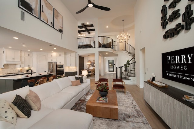 living room featuring wood-type flooring, beamed ceiling, ceiling fan with notable chandelier, and a high ceiling