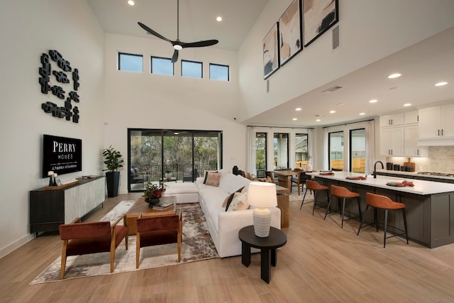 living room featuring light hardwood / wood-style flooring, a towering ceiling, ceiling fan, and sink