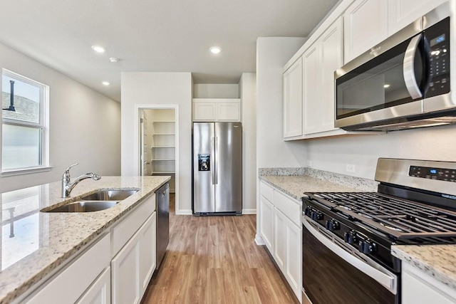 239 Spirit St, Elgin, TX 78621 - kitchen with stainless steel appliances, a sink, light wood-style flooring, white cabinetry, and light stone countertops