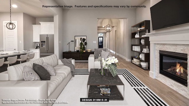 living room with an inviting chandelier, light hardwood / wood-style floors, and a stone fireplace