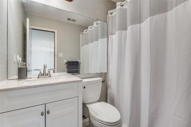 bathroom with visible vents, toilet, vanity, and a textured wall