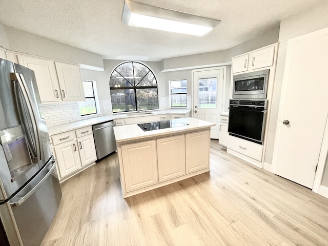 kitchen featuring black appliances, light countertops, light wood-style floors, backsplash, and a center island