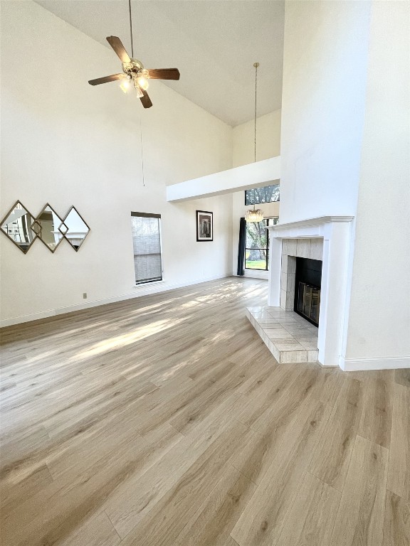 unfurnished living room featuring light hardwood / wood-style floors, high vaulted ceiling, ceiling fan, and a tiled fireplace