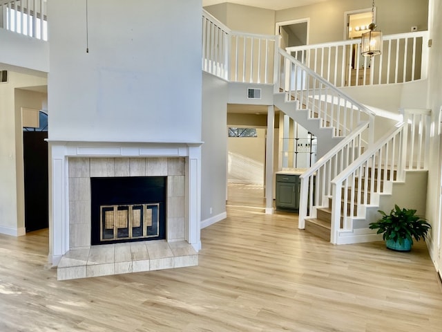 unfurnished living room featuring hardwood / wood-style floors, a towering ceiling, and a tiled fireplace