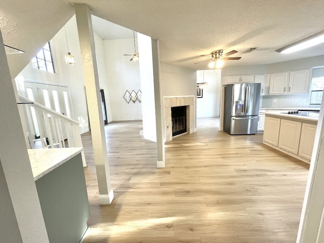 kitchen featuring backsplash, white cabinets, a fireplace, a textured ceiling, and stainless steel fridge with ice dispenser