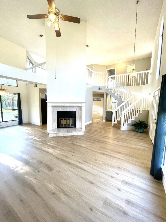 unfurnished living room featuring a towering ceiling, light hardwood / wood-style floors, a textured ceiling, a fireplace, and ceiling fan with notable chandelier