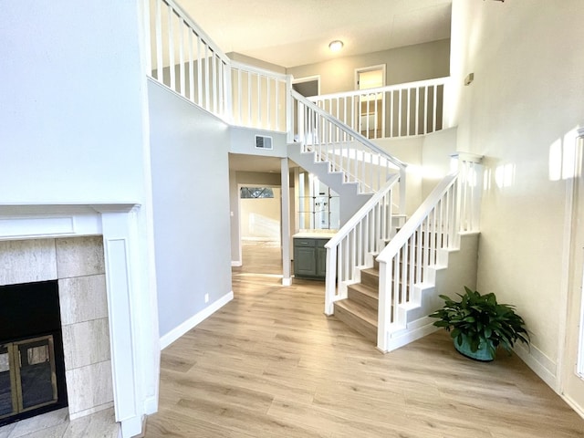 staircase with visible vents, baseboards, a tile fireplace, a towering ceiling, and wood finished floors