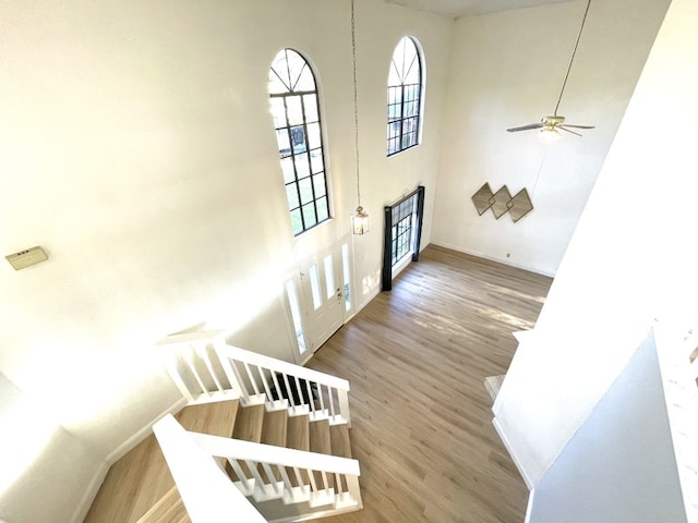 stairs with ceiling fan, baseboards, a towering ceiling, and wood finished floors