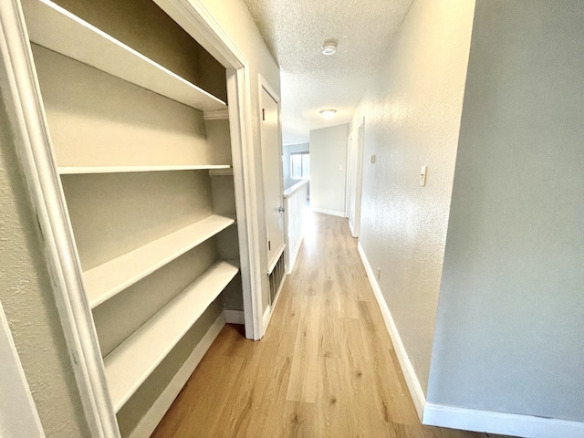 hall with light wood-type flooring and a textured ceiling