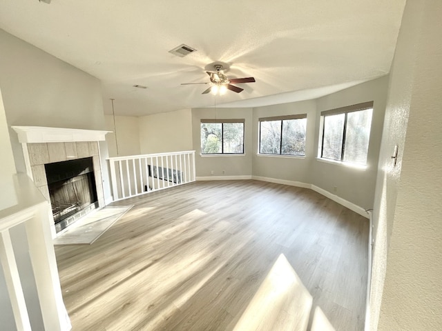 unfurnished living room featuring a tile fireplace, ceiling fan, and light wood-type flooring