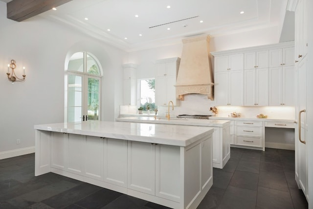 kitchen featuring light stone counters, premium range hood, a kitchen island, backsplash, and white cabinetry