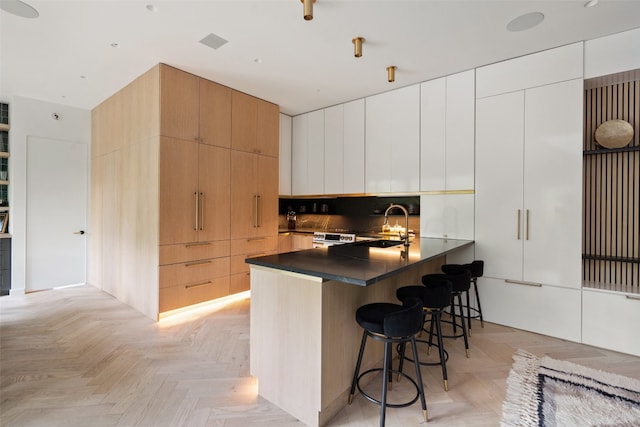 kitchen featuring sink, kitchen peninsula, white cabinetry, light parquet floors, and a kitchen bar