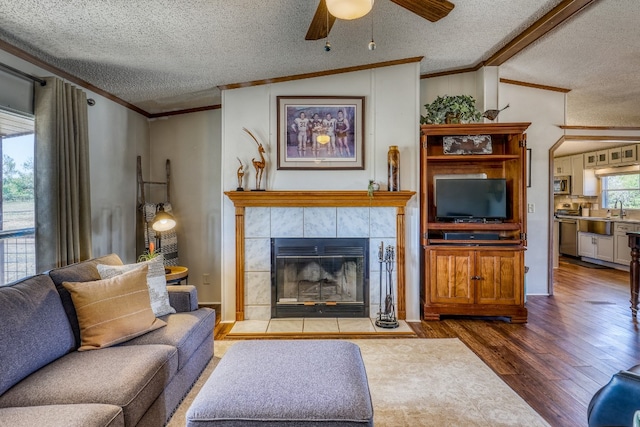 living room with lofted ceiling with beams, a textured ceiling, a tile fireplace, hardwood / wood-style flooring, and ceiling fan