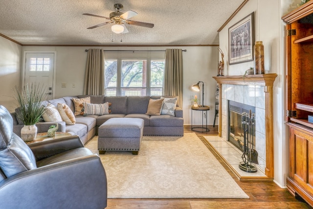 living room featuring a tile fireplace, a textured ceiling, wood-type flooring, ceiling fan, and ornamental molding