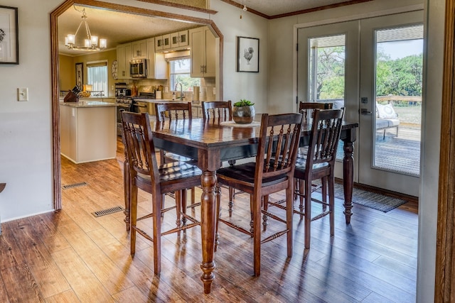 dining space featuring a notable chandelier, light wood-type flooring, crown molding, and a healthy amount of sunlight