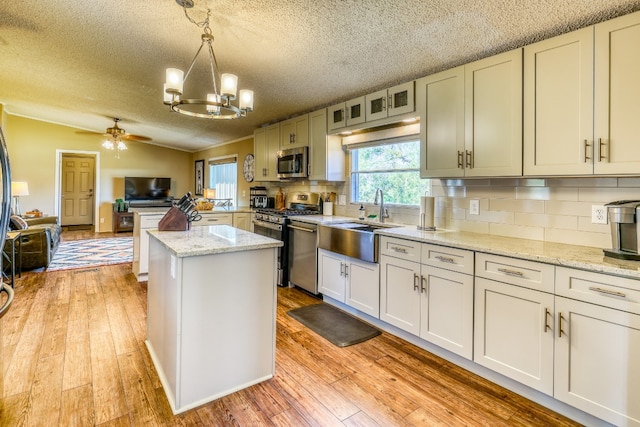 kitchen featuring appliances with stainless steel finishes, pendant lighting, light hardwood / wood-style flooring, and light stone counters