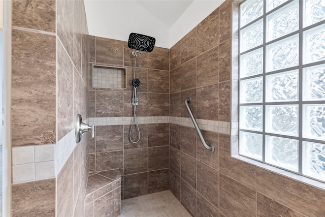 bathroom with a tile shower, lofted ceiling, and plenty of natural light