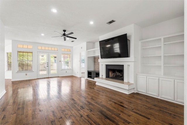 unfurnished living room featuring built in shelves, ceiling fan, and dark hardwood / wood-style flooring