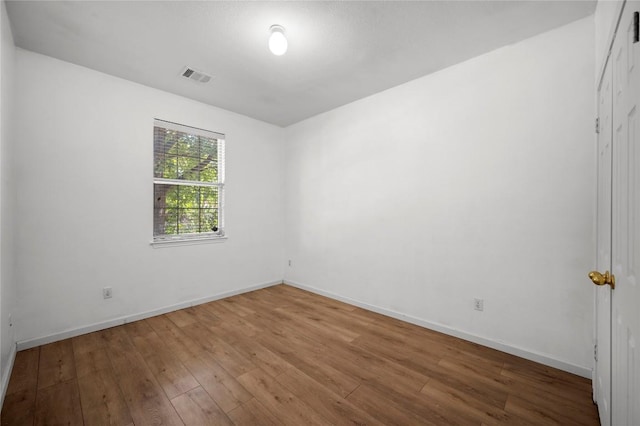 unfurnished room with baseboards, wood finished floors, and visible vents