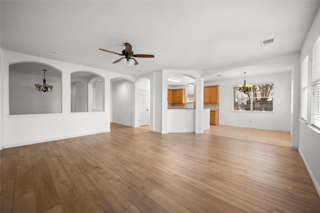 unfurnished living room featuring ceiling fan with notable chandelier and light hardwood / wood-style floors