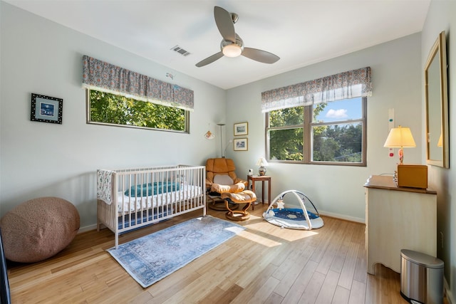 bedroom with light hardwood / wood-style flooring, a nursery area, and ceiling fan