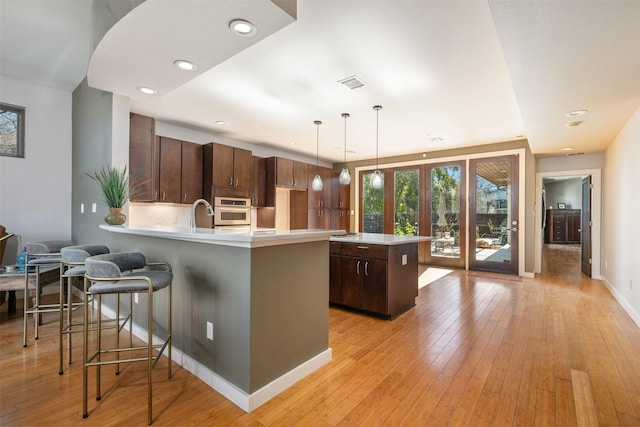 kitchen with dark brown cabinetry, hanging light fixtures, light wood-type flooring, kitchen peninsula, and backsplash