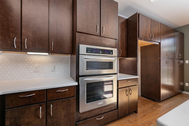 kitchen with decorative backsplash, double oven, dark brown cabinets, and light hardwood / wood-style flooring