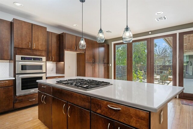 kitchen with dark brown cabinets, hanging light fixtures, light wood-type flooring, appliances with stainless steel finishes, and a kitchen island