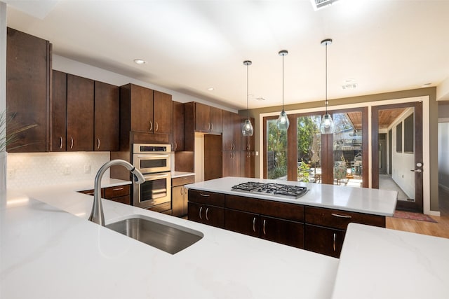 kitchen featuring sink, appliances with stainless steel finishes, tasteful backsplash, dark brown cabinetry, and decorative light fixtures