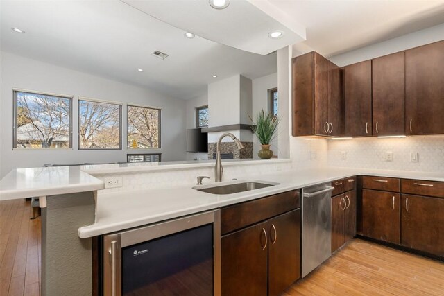 kitchen featuring sink, wine cooler, decorative backsplash, dark brown cabinetry, and kitchen peninsula