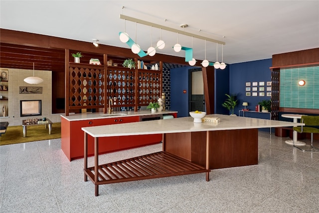 kitchen featuring a kitchen breakfast bar, a fireplace, a center island, decorative light fixtures, and sink