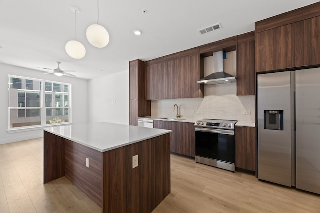 kitchen with tasteful backsplash, decorative light fixtures, light hardwood / wood-style flooring, wall chimney range hood, and appliances with stainless steel finishes