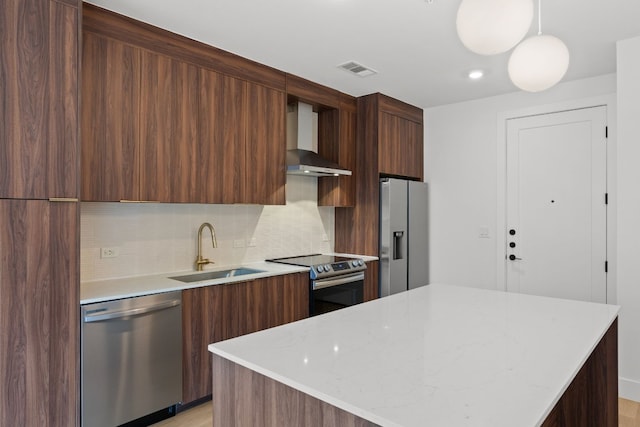 kitchen featuring light stone counters, sink, hanging light fixtures, wall chimney exhaust hood, and appliances with stainless steel finishes