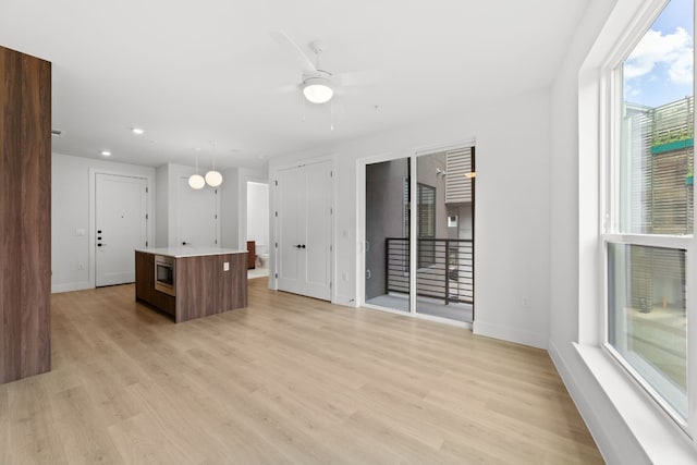 kitchen with light wood-type flooring, ceiling fan, a center island, and hanging light fixtures