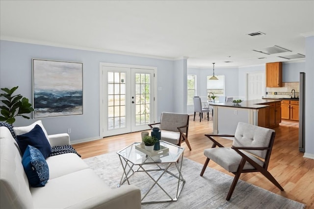 living area featuring baseboards, visible vents, light wood-style flooring, crown molding, and french doors