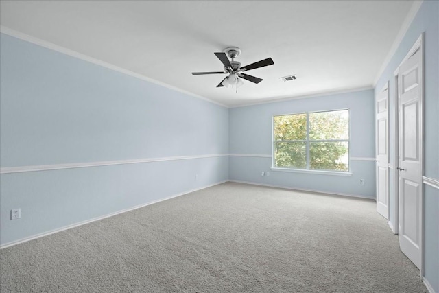 carpeted spare room featuring a ceiling fan, visible vents, crown molding, and baseboards