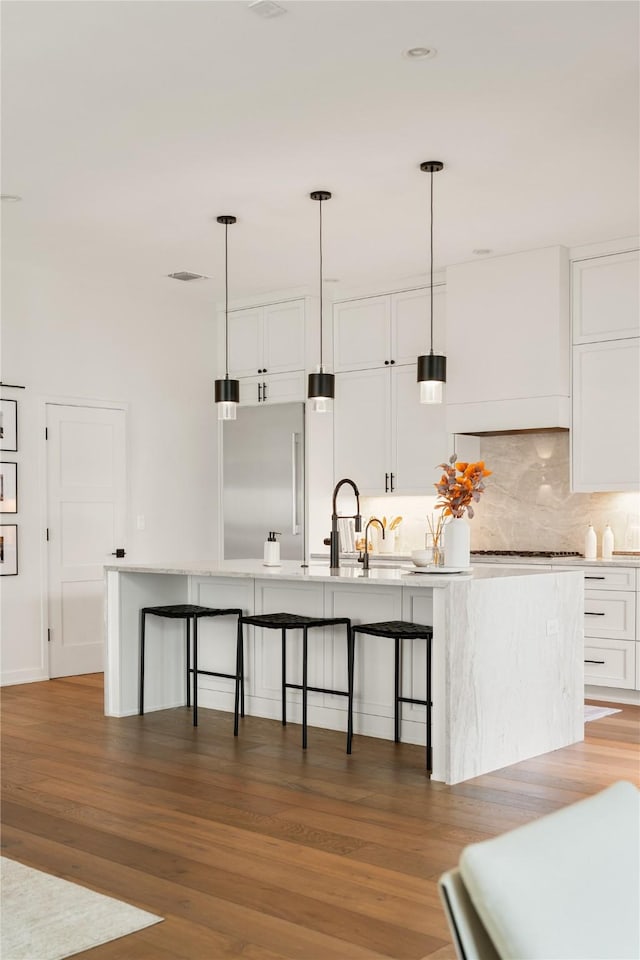 kitchen with white cabinetry, stainless steel built in fridge, a kitchen island with sink, and hanging light fixtures