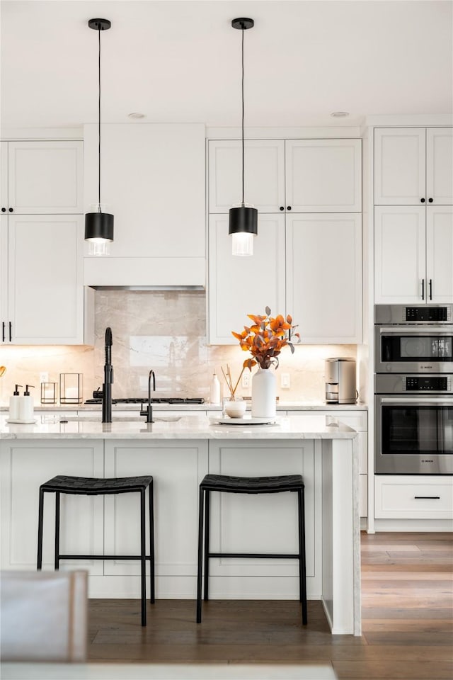 kitchen with double oven, decorative light fixtures, a breakfast bar area, and white cabinets